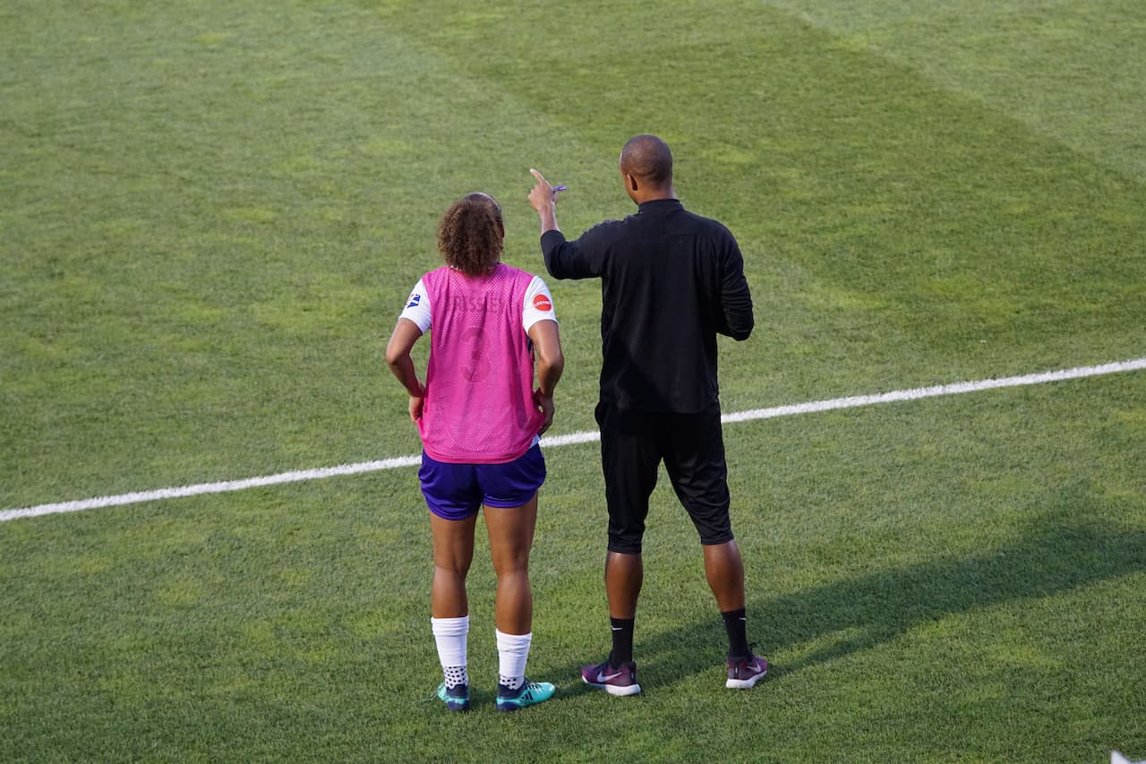 A man and a woman in a football field. The man is coaching the woman