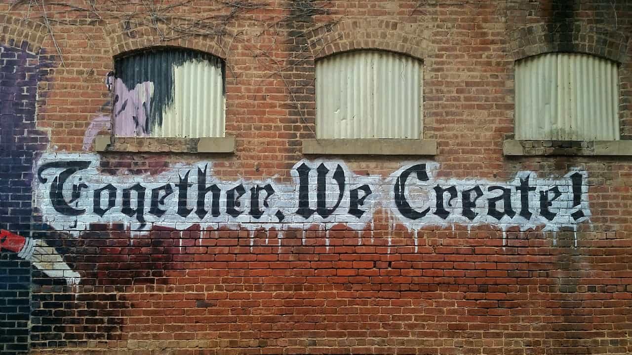 A brick wall that says "Together We Create" in Graffiti