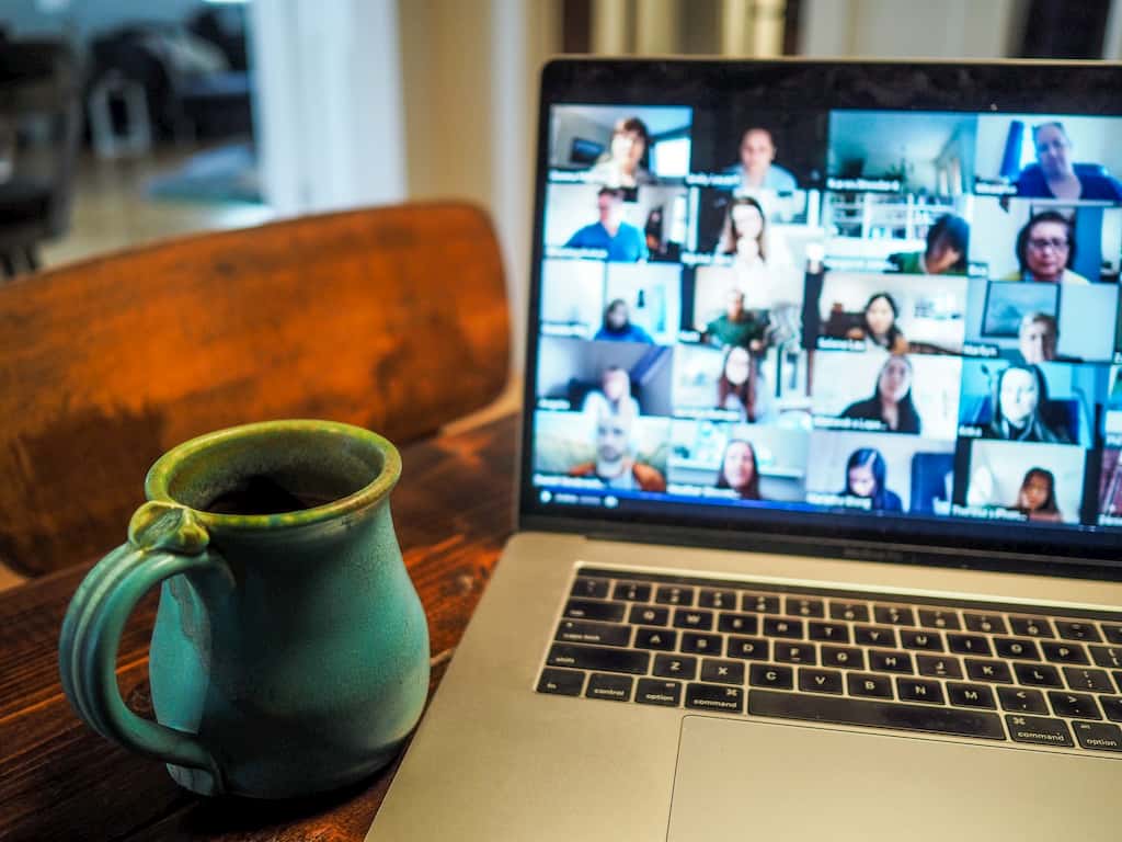 People in a video chat room having a meeting. A mug is on the left side and a computer with the video call is on the right