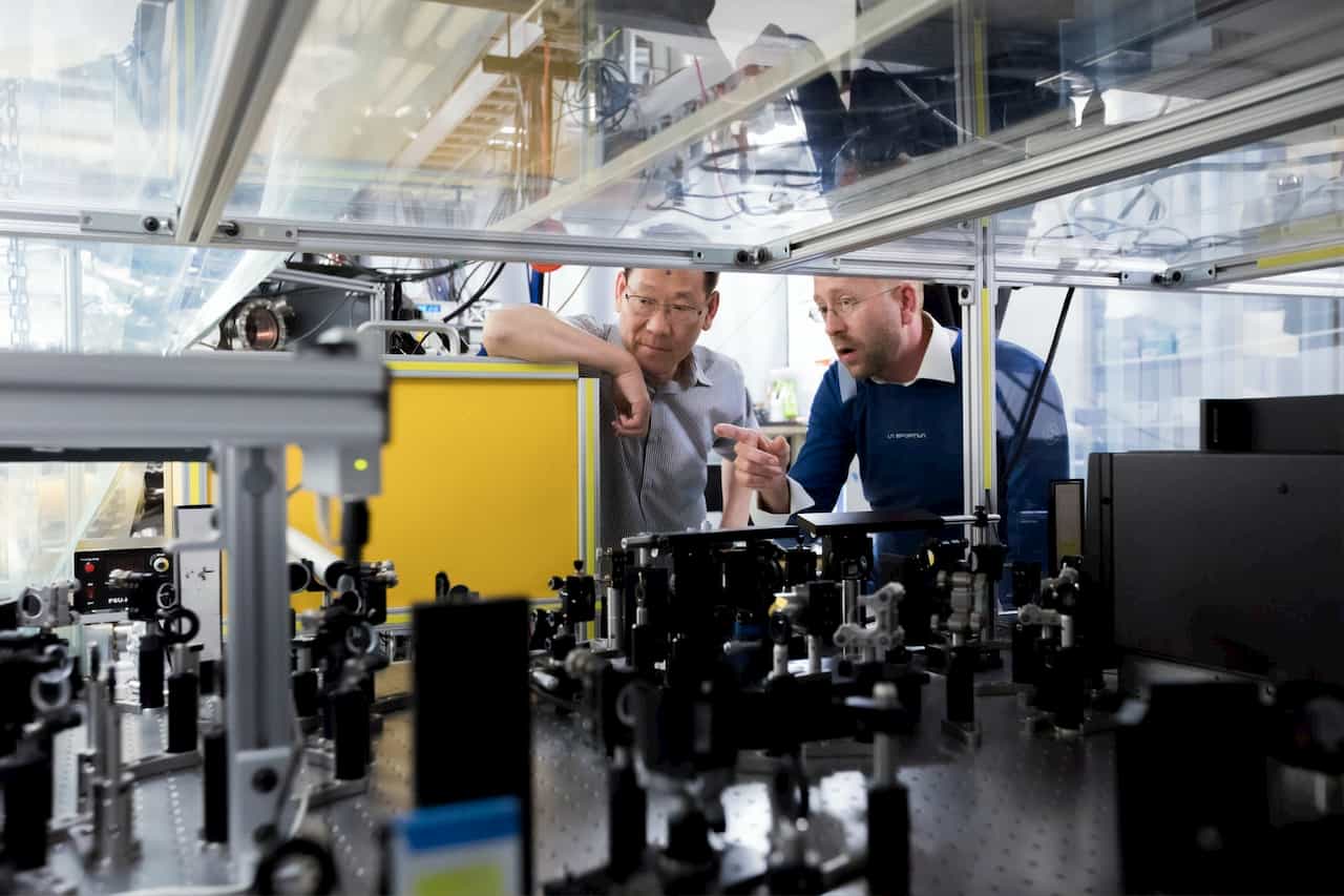 Two men having a conversation while look at the insides of machinery. One is speaking and both are looking at the machines