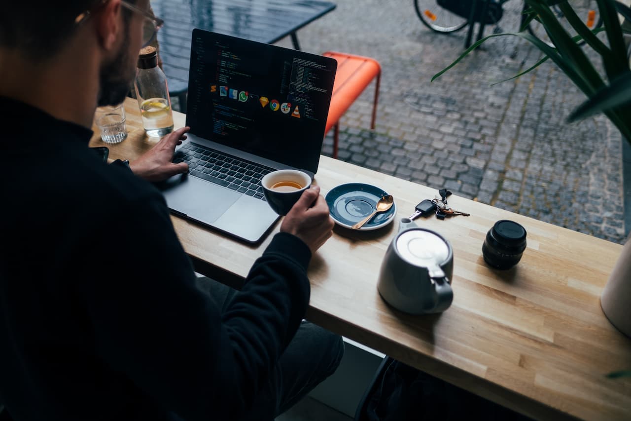 Man with a Mac working in a Café. The man has multiple apps open and is doing a command+tab shifting from one to the other